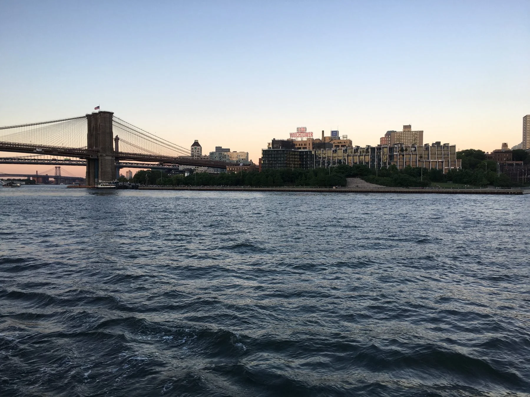 The Brooklyn Bridge over the East River at dusk, with Brooklyn buildings catching warm sunset light in the background